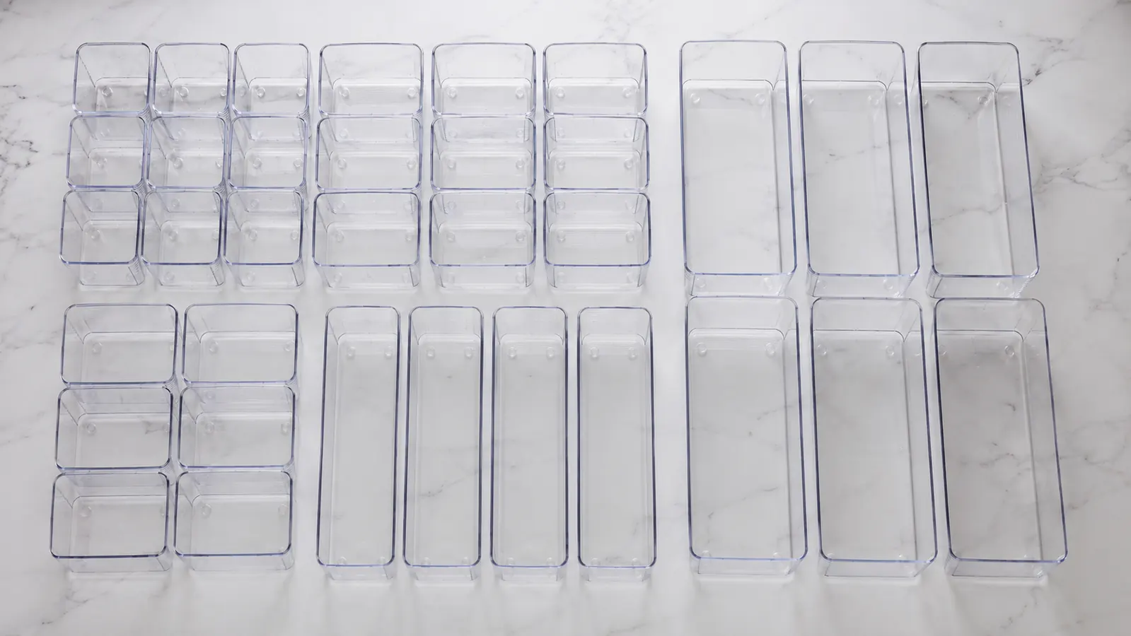 Clear plastic drawer organizer bin set laid out on a white countertop showing all four sizes