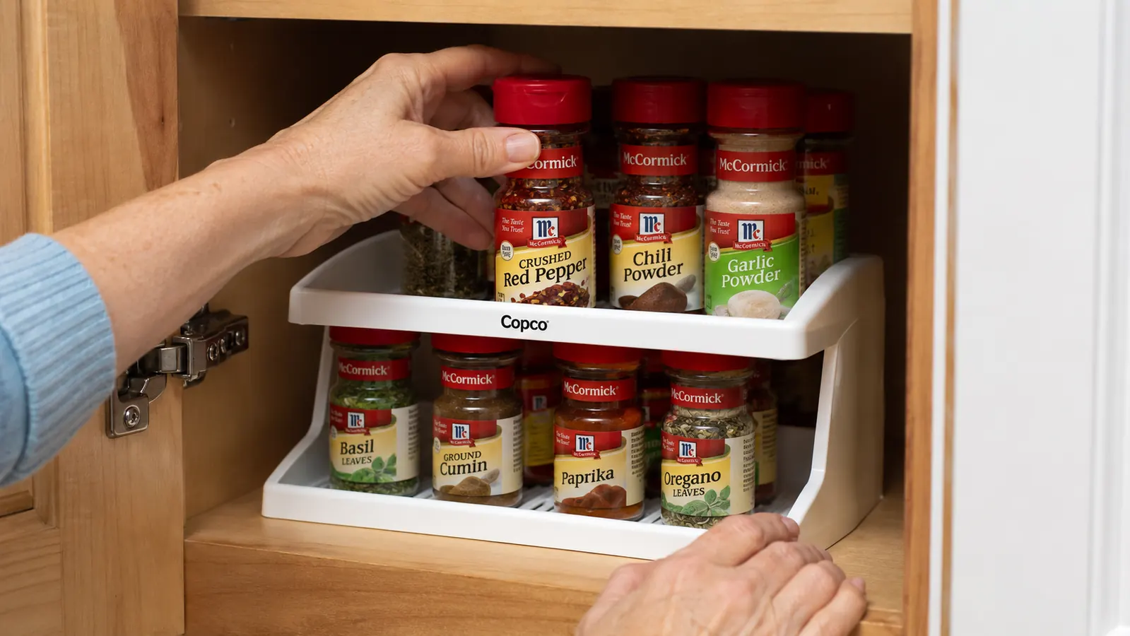 Hand placing a tall McCormick spice bottle on the top tier of a Copco spice rack to show height clearance