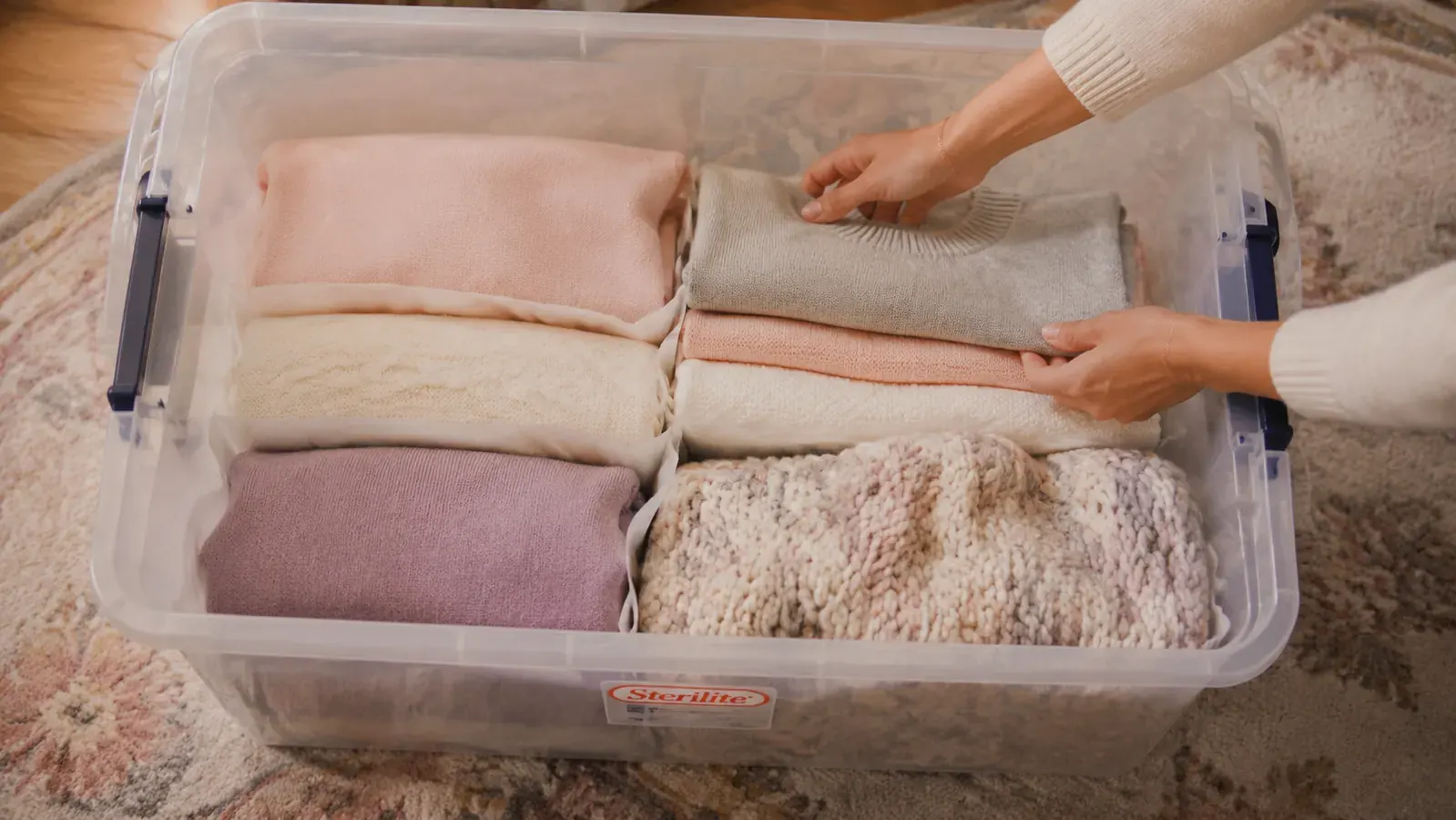 Neatly folded seasonal sweaters and blankets organized inside a clear under-bed bin